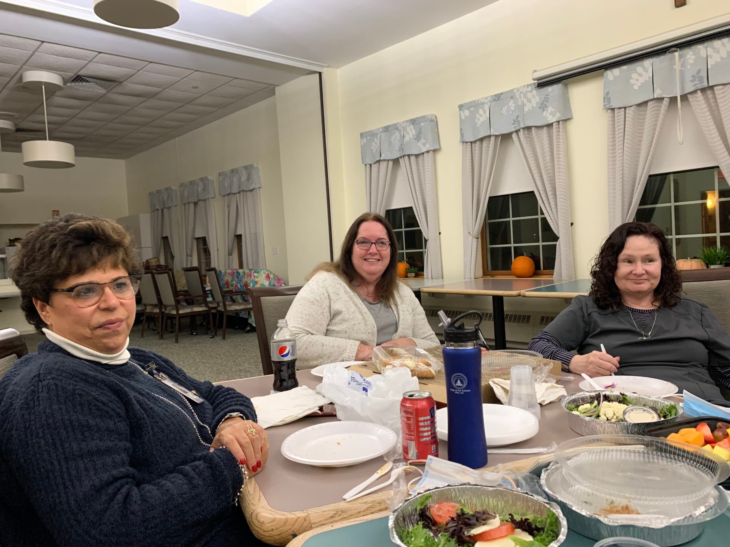 Three women sitting at a table with food.