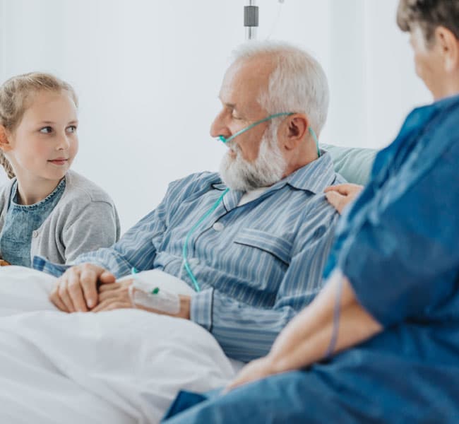 Two nurses sitting next to a veteran in a hospital bed