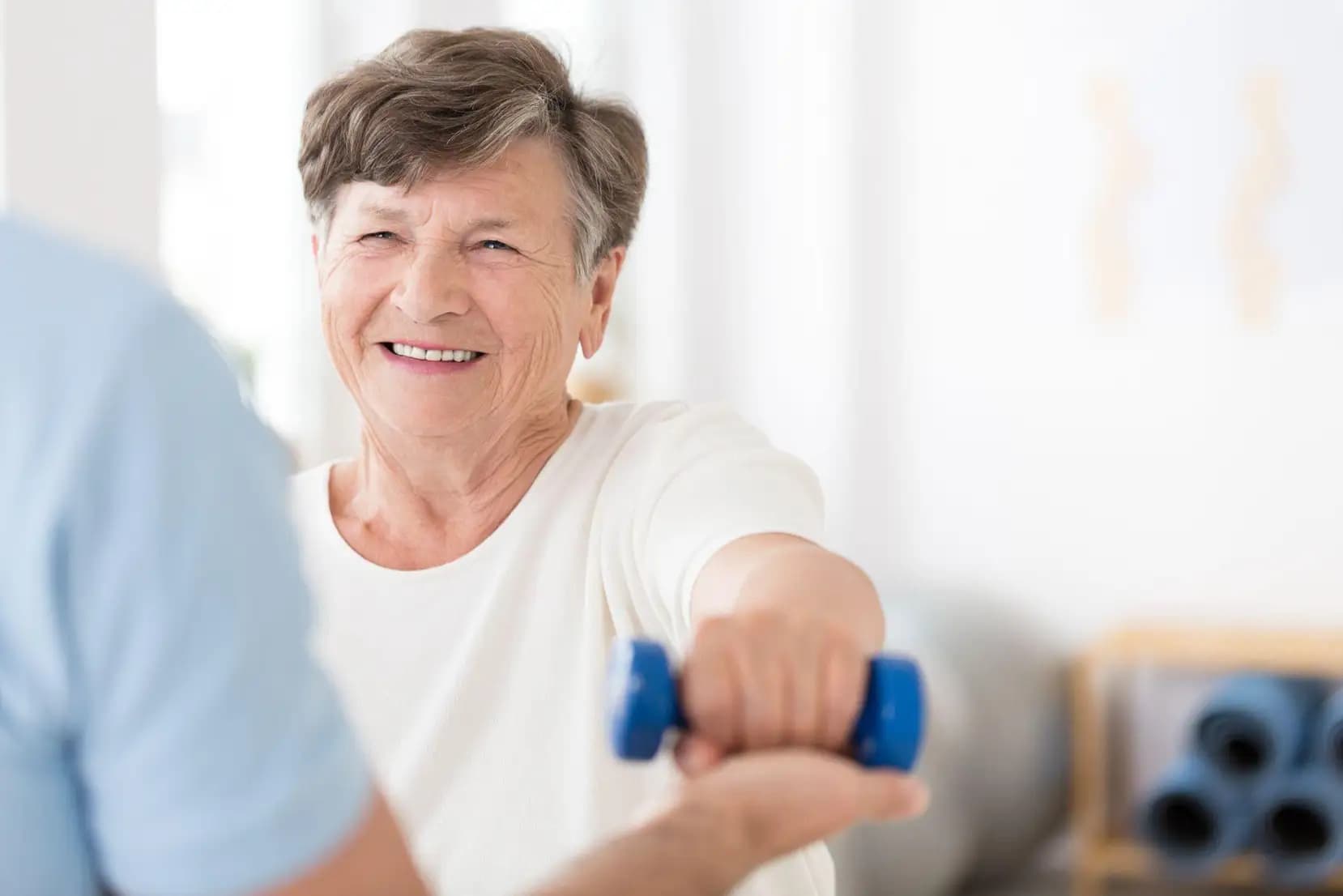 a senior woman holding weights with the help of her fitness trainer