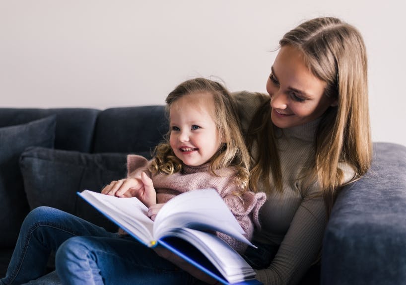 happy-mother-little-daughter-reading-book-sitting-comfortable-couch-living-room