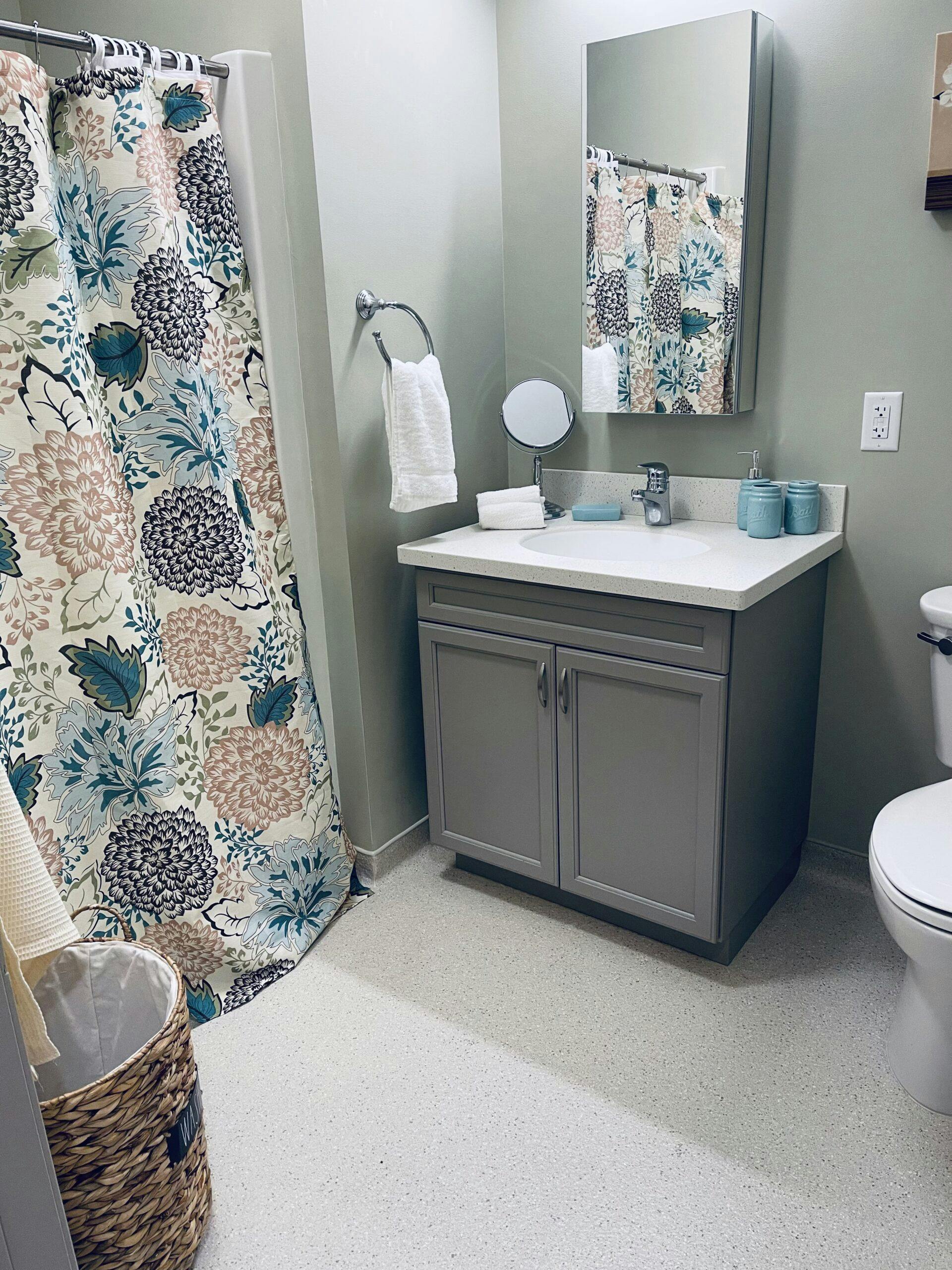 An assisted living bathroom with a sink, toilet, and shower curtain.