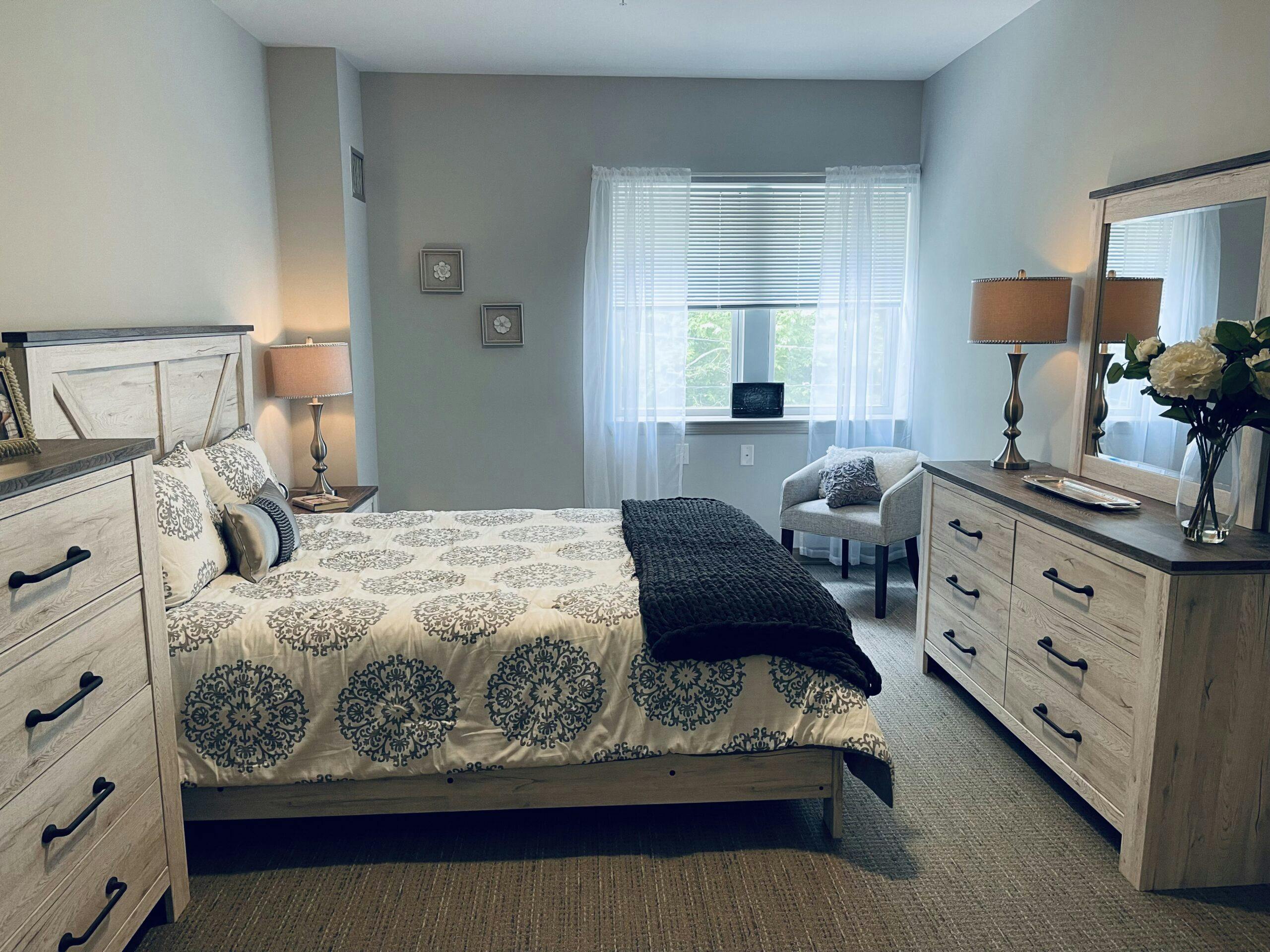 An assisted living bedroom with a bed, dresser, and mirror.